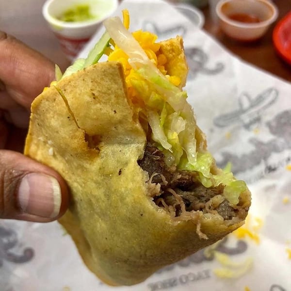 A hand holds a partially eaten Roberto's Taco Shop taco with meat, cheese, and lettuce.