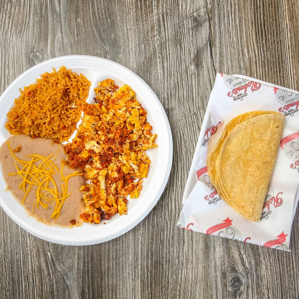 A plate of Mexican food with rice, refried beans, scrambled eggs with chorizo, and two tacos.