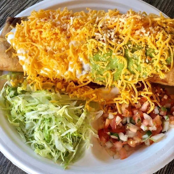 A Roberto's Taco Shop burrito covered in cheese, sour cream, and guacamole, with shredded lettuce and pico de gallo.