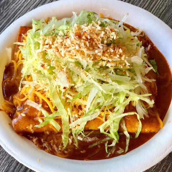 Roberto's Taco Shop enchiladas covered in red sauce, shredded cheese, lettuce, and cotija cheese.